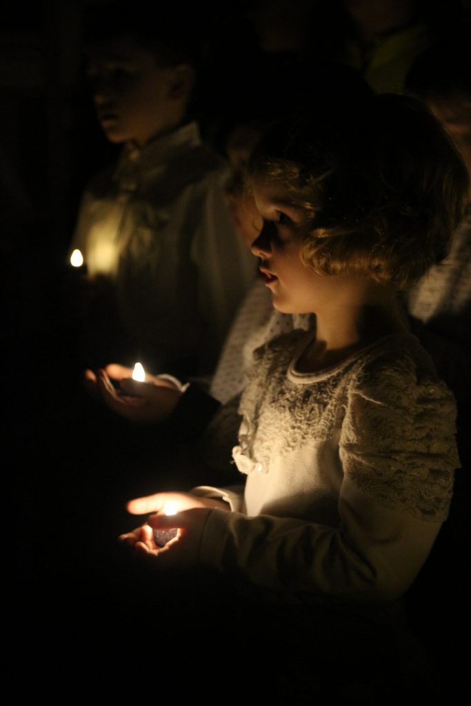Deti oblečené v anjelskom oblečení a v rúčkach majú malú sviečku. Svetlo vytvára iba žiara ich sviečok.