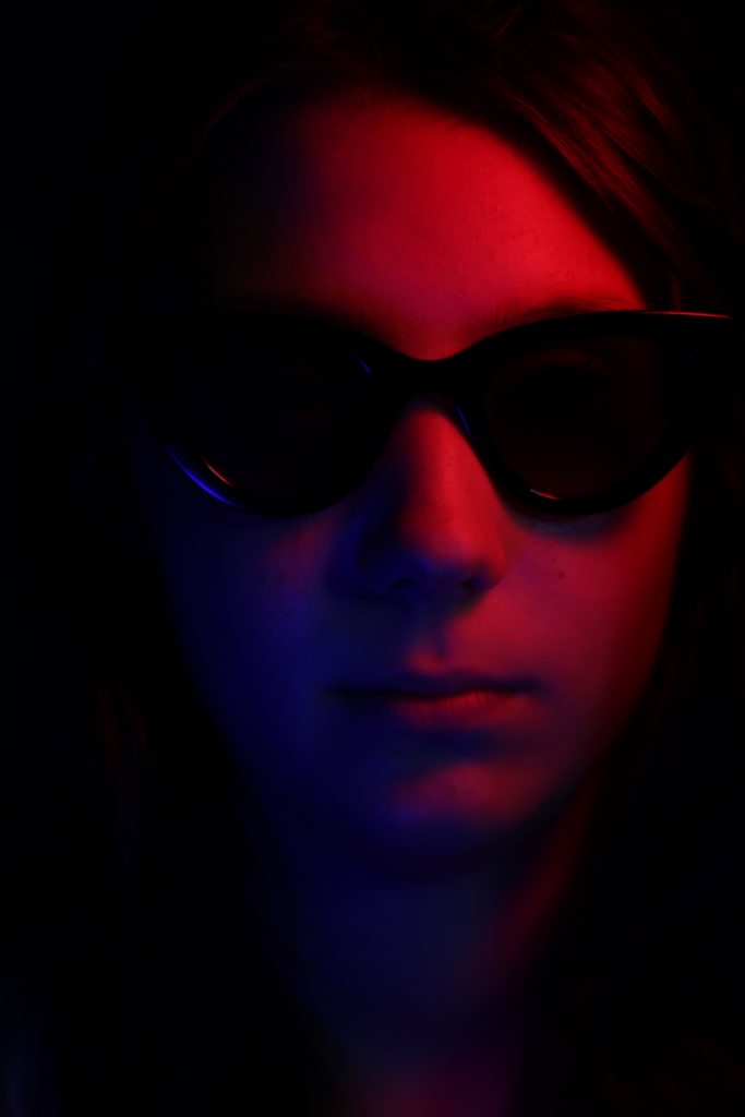 Portrét dievčaťa v slnečných okuliaroch. Tvár je osvetlená dočervena.