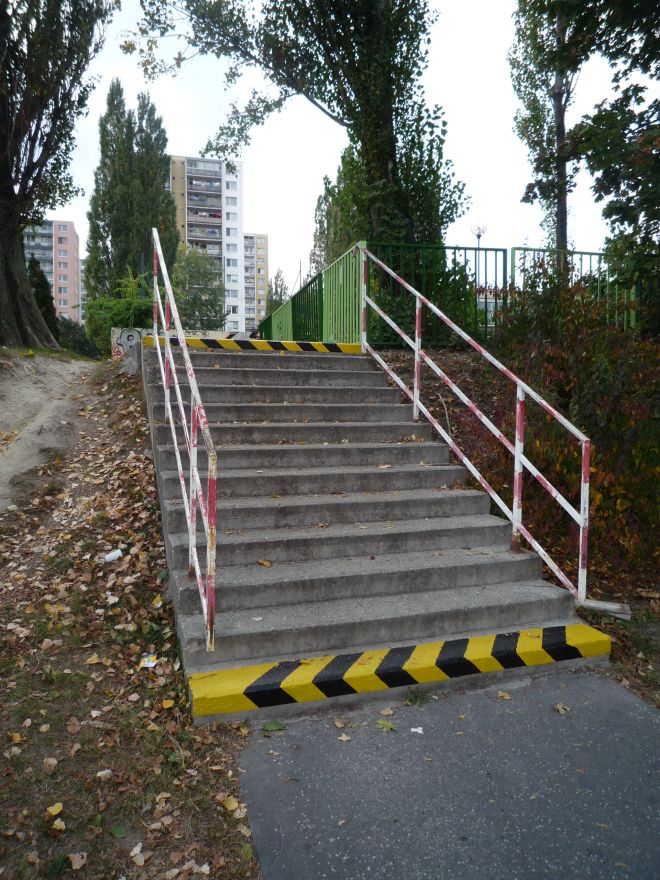 Záber na schodisko, ktoré sa nachádza na sídlisku. Prvý a posledný schod je označený čierno-žltým značením. Po stranách schodiska je bielo-červené zábradlie.