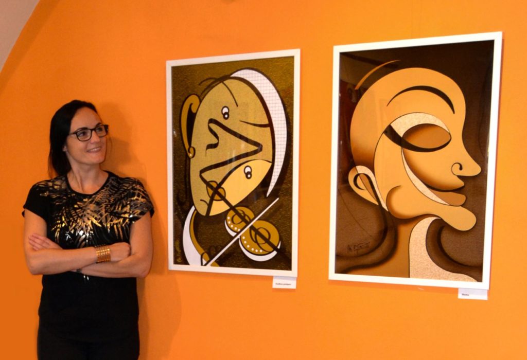 Na obrázku je usmiata autorka a díva sa na dva svoje obrazy. Ide o portréty, ktorým dominuje oranžovo-hnedá farba. Tváre sú tvorené rôzne zakrútenými líniami.