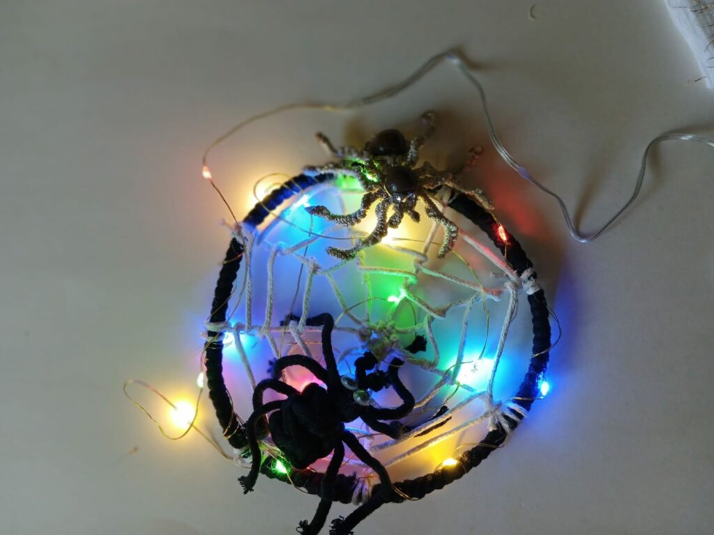 Na obrázku je kruh, ktorý tvorí pavučinu a v nej pavúk. V pavučine sú aj farebné svetielka. 