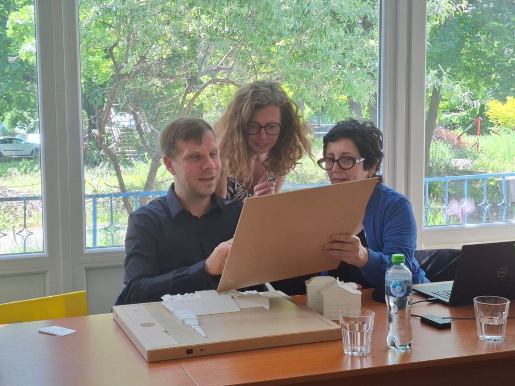 Na obrázku sú všetci traja zástupcovia EBU, Lars Bosselmann a Valérie Bertrand-Vivancos sedia za stolom. V rukách držia hovoriaci rám. Nad nimi stojí Andrea Bila - všetci traja sa so záujmom dívajú na pamiatku vyobrazenú na ráme. Lars je nevidiaci, takže má na reliéfnom obrázku ruku.